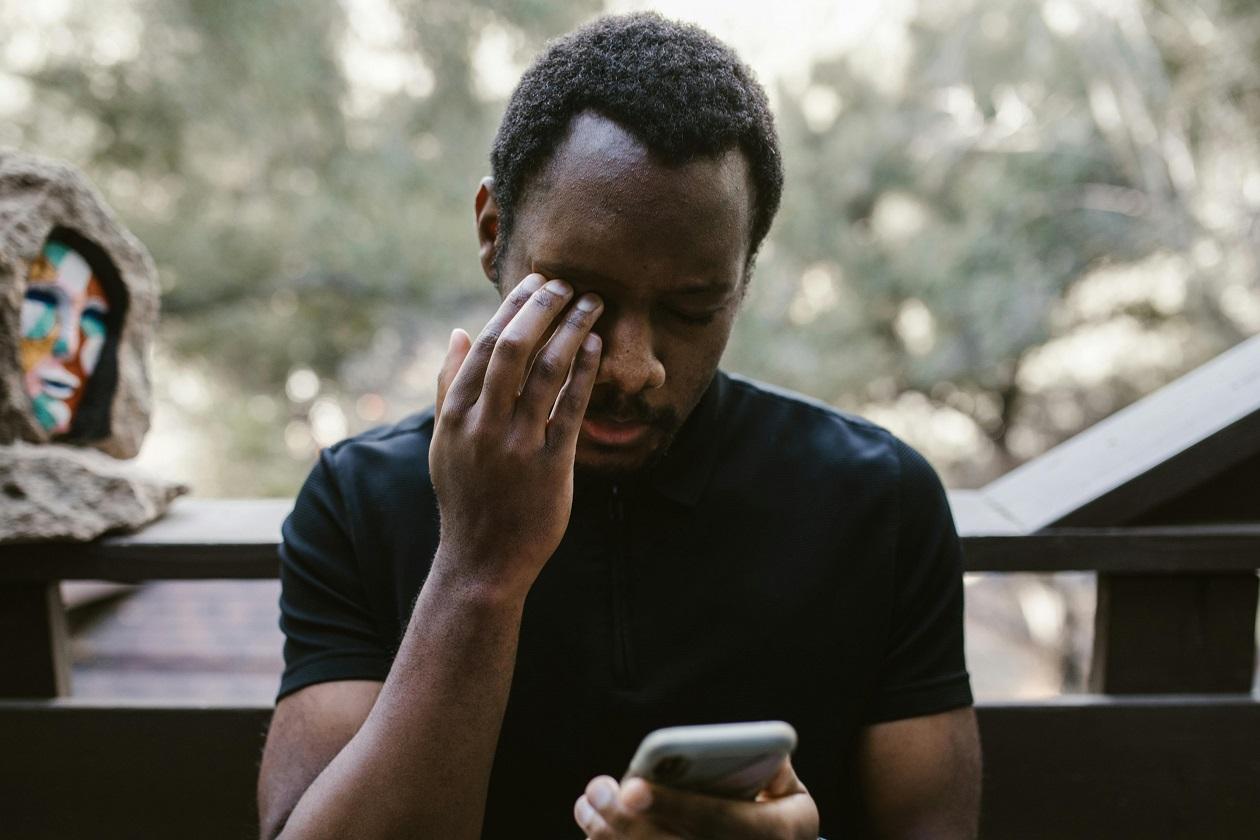 A man on his phone while wiping his eye